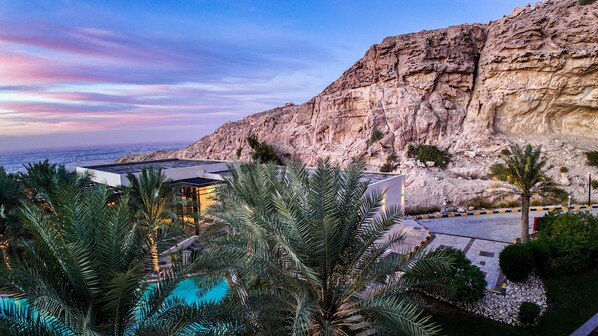A resort with a pool, palm trees, and a rocky cliff backdrop. - Alberni Jabal Hafeet Hotel (Al Ain)