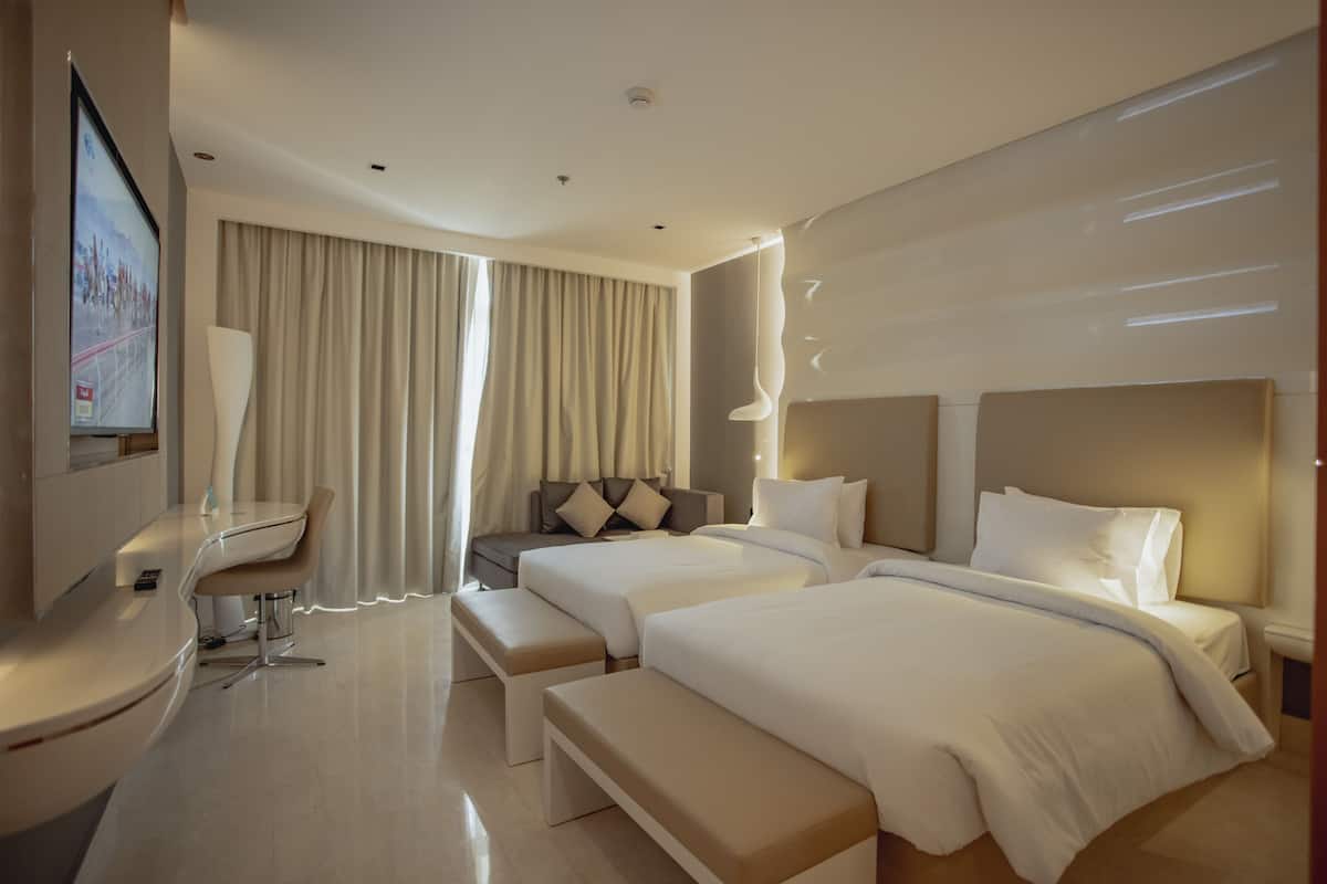 Una habitación de hotel moderna con dos camas, un escritorio y un amplio ventanal con cortinas.