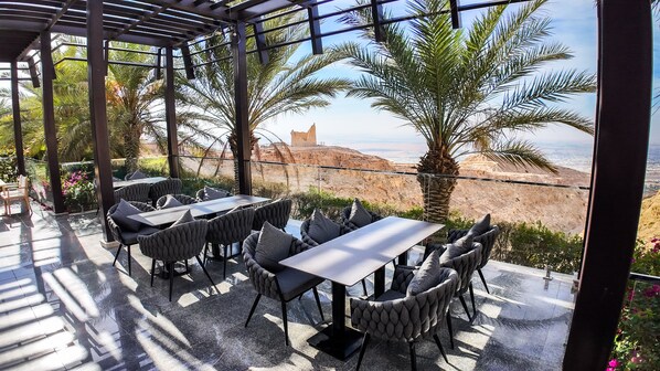Un patio al aire libre con mesas y sillas, con vistas a un paisaje rocoso y un cielo despejado.