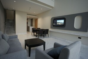 A modern living room with a flat-screen TV mounted on the wall, a dining area with a table and chairs, and a staircase leading to another level. - Alberni Jabal Hafeet Hotel (Al Ain)