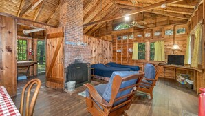 A rustic cabin interior with a brick fireplace, two beds, a dining table, and a work desk.