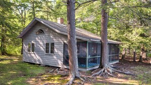 A rustic cabin with a sloped roof, large windows, and a screened porch.