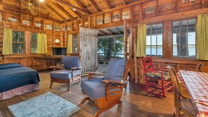 A cabin with wooden walls and a ceiling fan, furnished with two beds, a dining table, and several chairs.