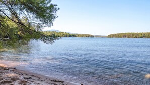 A lake with a sandy beach and trees in the foreground.
