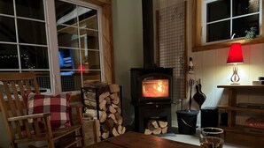 En hyggelig stue med pejs, en gyngestol i træ, et bord med et glas vin og et vindue med udsigt over byen om natten.