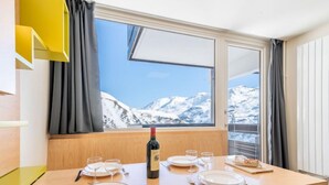 A dining table set with plates, glasses, and cutlery, a bottle of wine, and a view of snow-capped mountains through a window. - Home Club (Lavachet) by Interhome (Tignes)