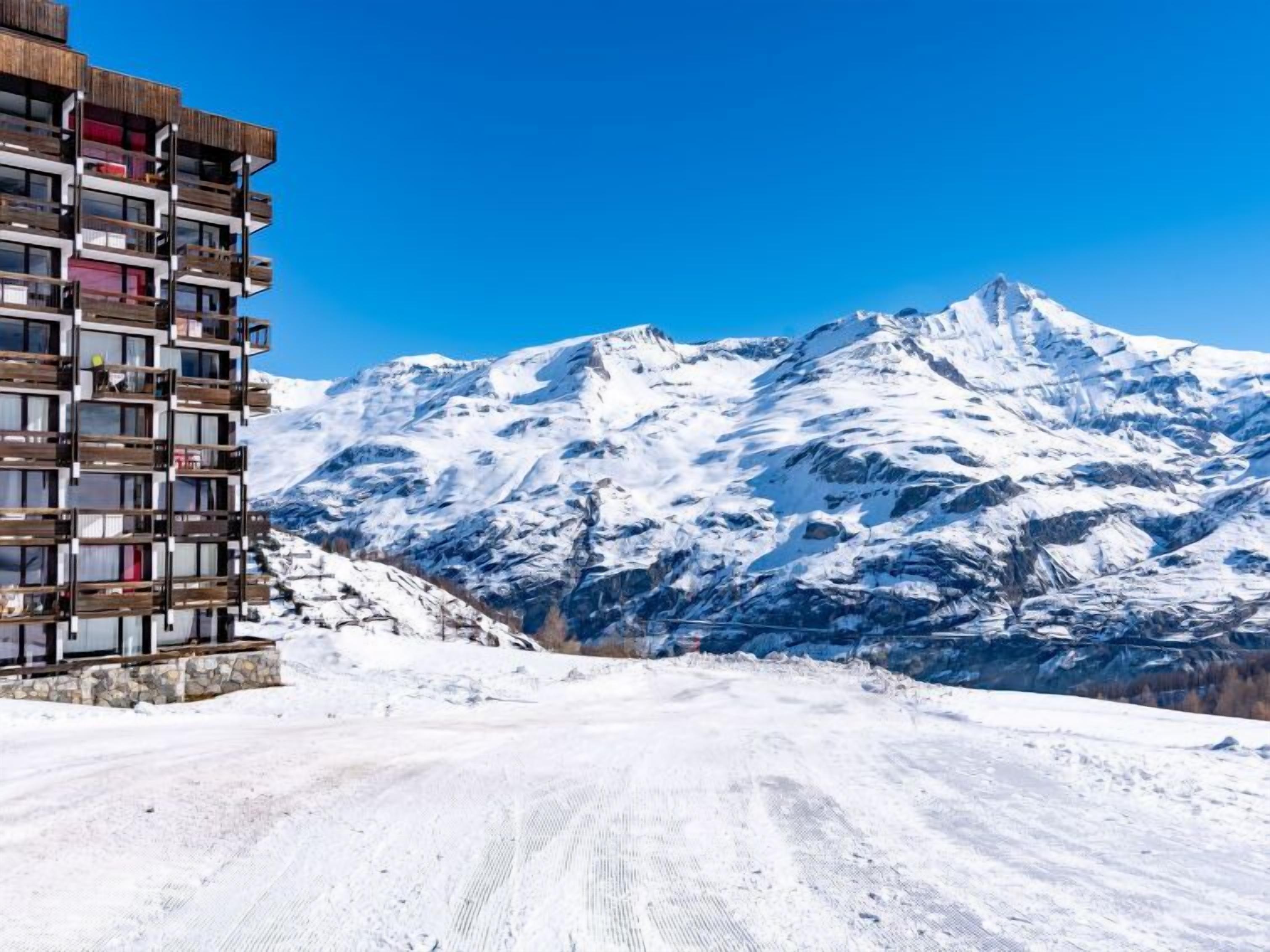 A modern building with multiple balconies overlooking a snow-covered mountain range.