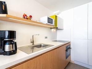A modern kitchen with a stainless steel sink, a coffee maker, and a microwave on a shelf.