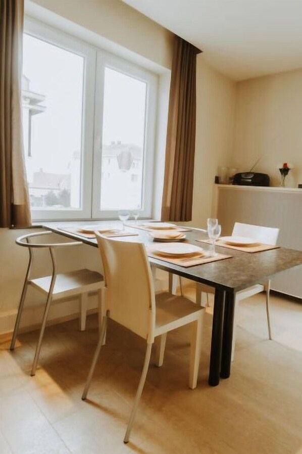 A dining area with a table set for two, two chairs, and a window with curtains.