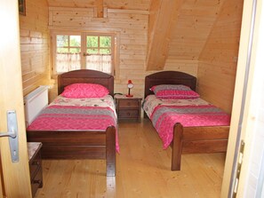 A cozy cabin room with two wooden beds, a small bedside table with a lamp, and a window with curtains. - Holiday Home Ena (Plitvicka Jezera)