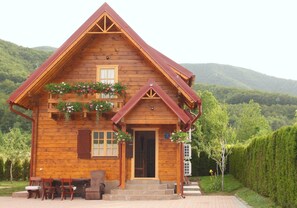 A wooden cabin with a steep roof, a front porch with chairs, and flower boxes. - Holiday Home Ena (Plitvicka Jezera)