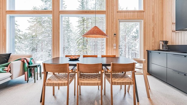 A modern dining area with a large wooden table, four chairs, and a woven pendant light.