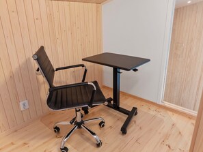 A room with a wooden floor, a black office chair with wheels, and a small black table.