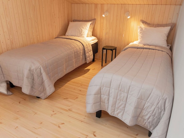 A room with two beds, wooden walls, and a small table.