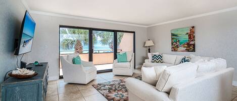 A living room with a large window, a flat-screen TV, a sofa set, and a painting on the wall.