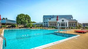 A swimming pool with clear blue water, surrounded by lounge chairs and umbrellas, with a building in the background. - Baywatch II 102A at Heron Harbour by Seaside Vacations & Sales (Ocean City)