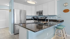 A modern kitchen with white cabinets, stainless steel appliances, and a granite countertop. - Baywatch II 102A at Heron Harbour by Seaside Vacations & Sales (Ocean City)