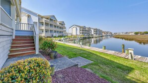 A waterfront hotel with multiple balconies, a dock, and a calm water body. - Baywatch II 102A at Heron Harbour by Seaside Vacations & Sales (Ocean City)
