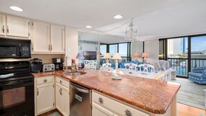 A modern kitchen with granite countertops, stainless steel appliances, and a view of the city through large windows.