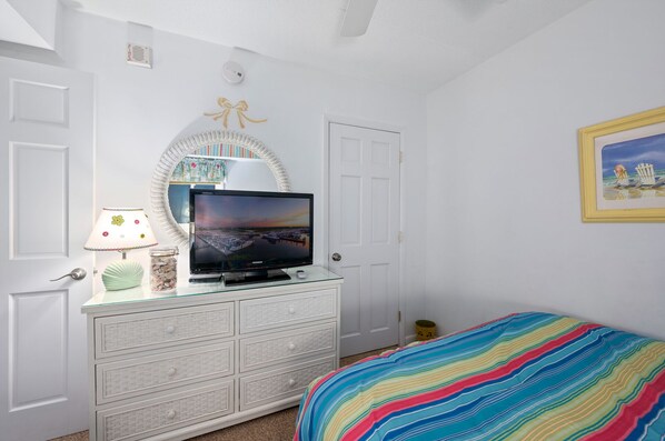 A bedroom with a television on a dresser, a bed with a colorful striped blanket, and a framed picture on the wall.