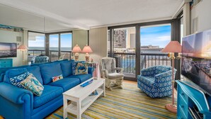 A modern living room with a blue sofa, patterned armchairs, and a television.