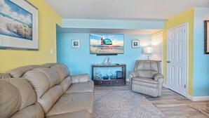 Una sala de estar con un sofá color crema, un sillón reclinable, un televisor en la pared y una alfombra estampada.