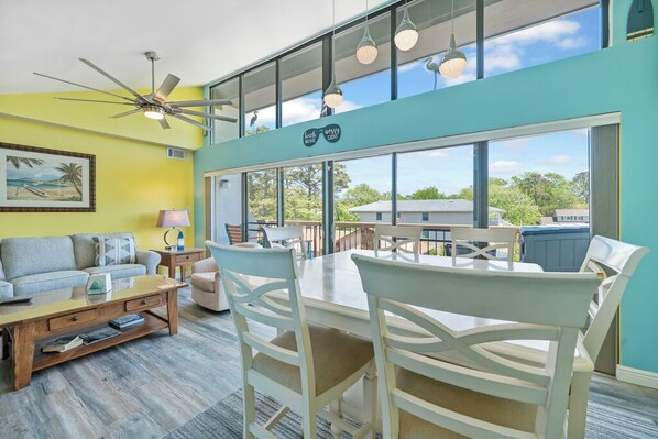 A bright living room with a ceiling fan, a dining table with chairs, a sofa, and a coffee table.