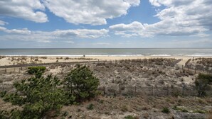 Una playa con una valla de madera, dunas arenosas y cielo despejado.