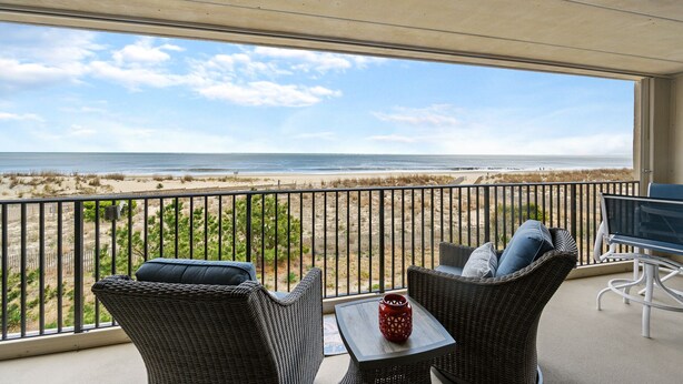 Un balcón con mobiliario de mimbre, una mesa y vistas a la playa y al océano.