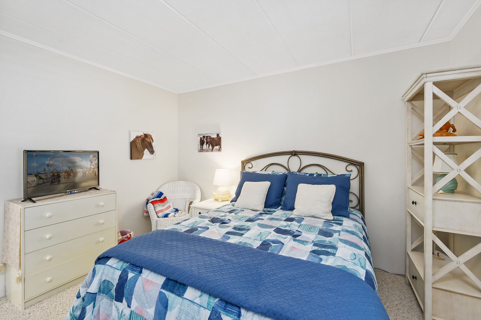 Een slaapkamer met een bed, een kaptafel, een nachtkastje, een lamp en een aan de muur bevestigde televisie.