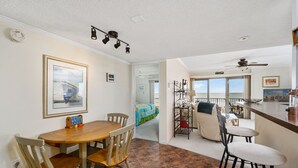 Un comedor con mesa y sillas de madera, una zona de cocina con barra y un balcón con vistas.