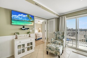 A living room with a TV, a sofa, a cabinet, and a balcony with a view. - Stunning condo w/ Bayfront indoor pool by Seaside Vacations & Sales (Ocean City)