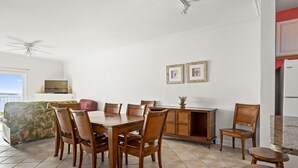 A dining area with a wooden table and chairs, a television on a stand, and framed pictures on the wall. - Maresol 502 by Seaside Vacations & Sales (Ocean City)