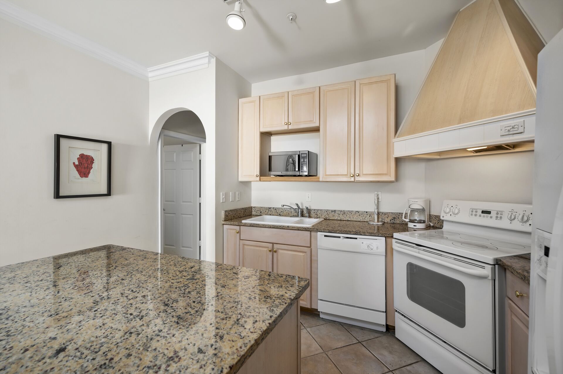 Una cocina con encimeras de granito, electrodomésticos blancos y armarios de madera clara.