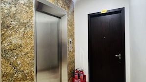 An elevator with a marble wall, a dark door, and a red fire extinguisher. - Sunrise Motel (Tuan Chau)