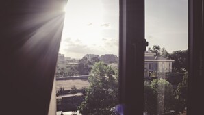 A view through a window with sunlight streaming in, featuring a building, trees, and a body of water. - Sunrise Motel (Tuan Chau)