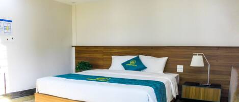 A modern hotel room with a wooden bed, a nightstand with a lamp, and a view of the outside.