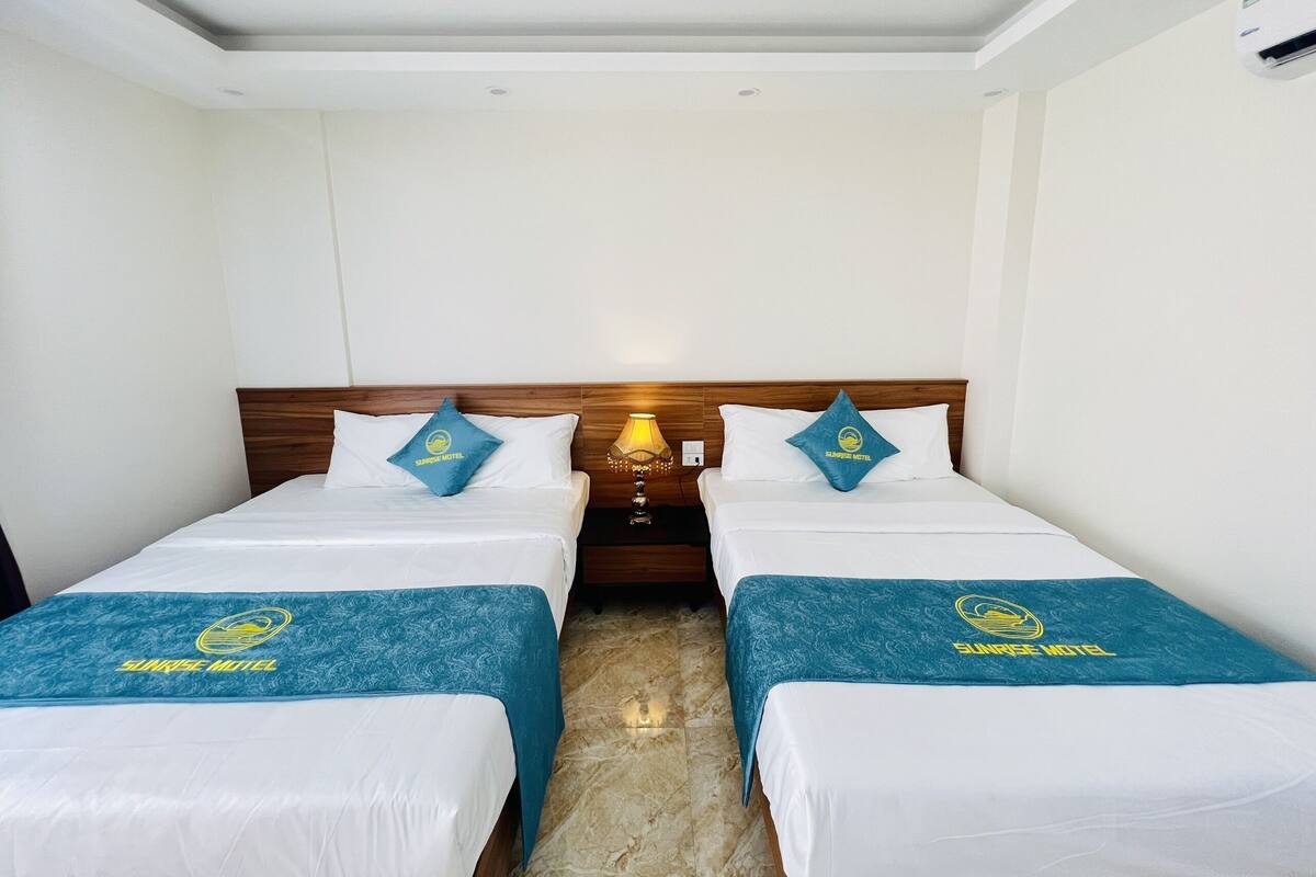 A hotel room with two beds, each with a blue bedspread and pillows featuring the Sunrise Motel logo.