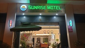 A hotel entrance with a sign for Sunrise Motel, outdoor seating area, and a visible balcony. - Sunrise Motel (Tuan Chau)