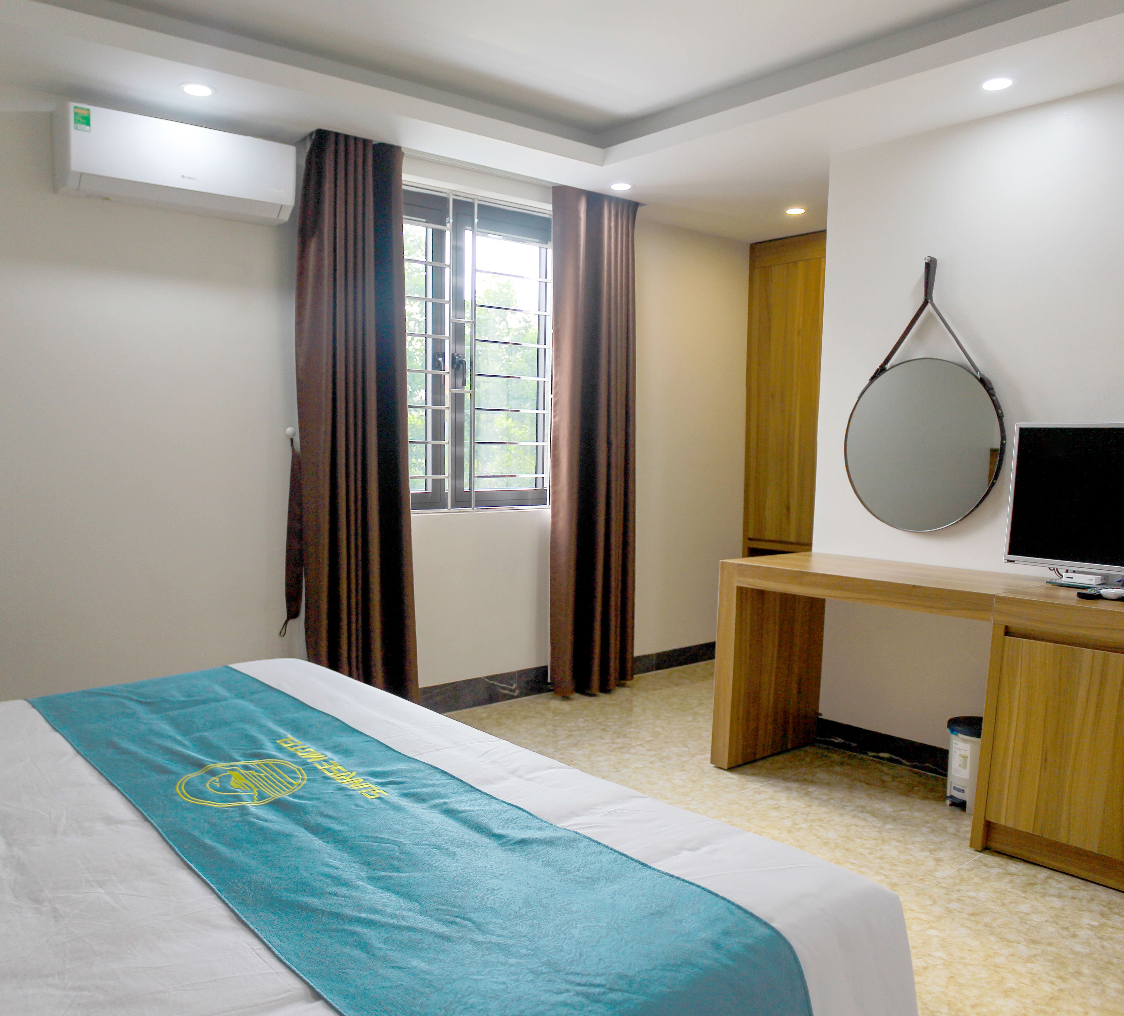 A hotel room with a bed, a desk, a television, and a window with curtains.