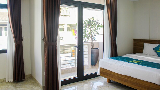 A hotel room with a bed, curtains, and a view of the outside balcony. - Sunrise Motel (Tuan Chau)
