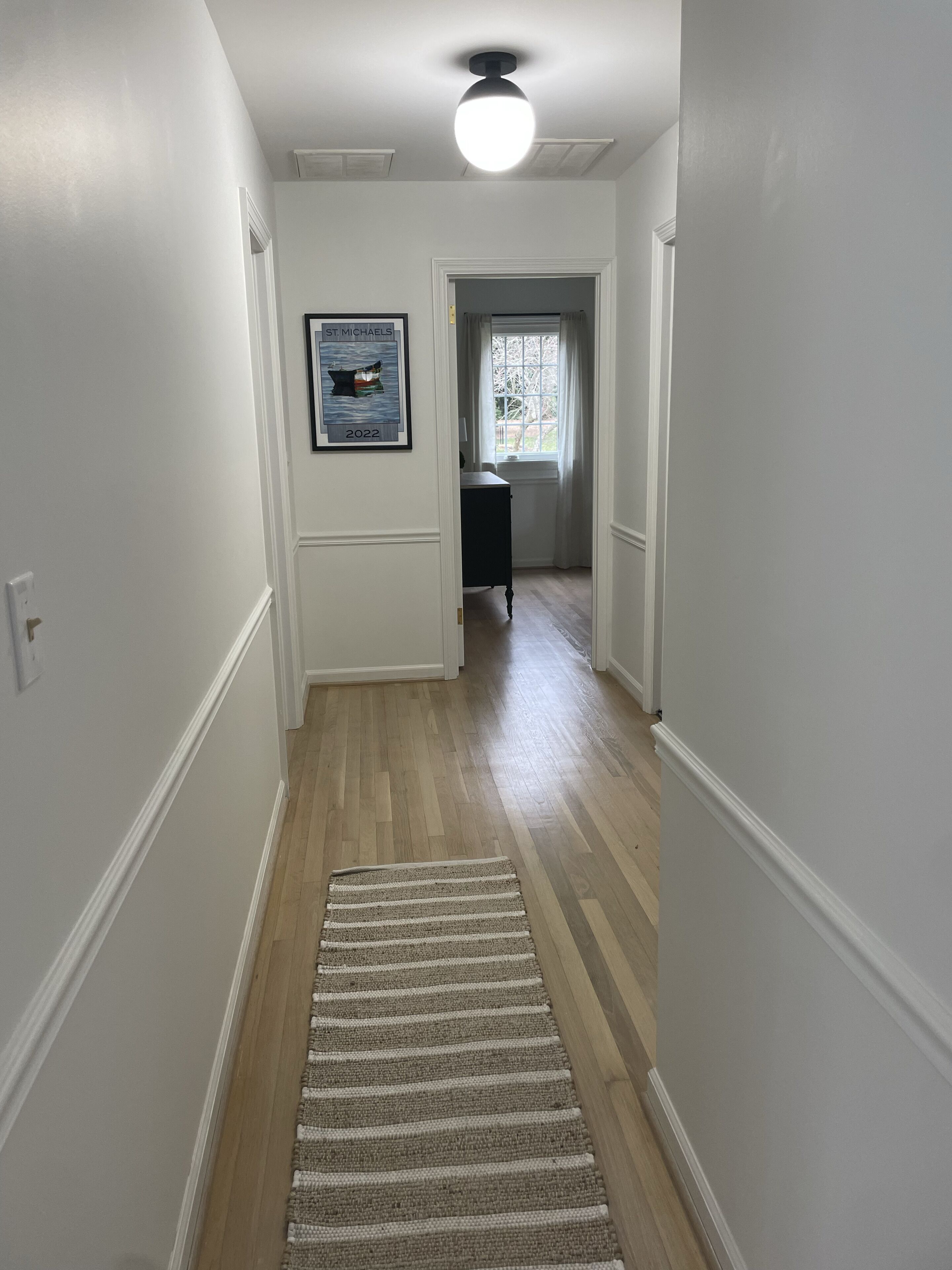 A hallway with wooden flooring, a striped rug, and a framed certificate on the wall.