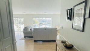 Ein geräumiger Wohnbereich mit einer Couch und einem Esstisch, großen Fenstern und Blick ins Freie.