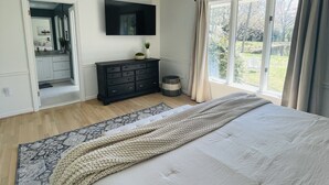 Ein Schlafzimmer mit einem großen Bett, einem an der Wand montierten Fernseher, einem Schminktisch und einem Fenster mit Vorhängen.
