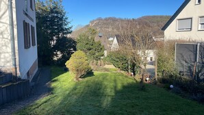 A residential area with a well-maintained lawn, a small garden, and a view of a hill with buildings in the background. - New, modern apartment with a great garden, centrally located - Bärs Kuschelhöhle (Gerolstein)