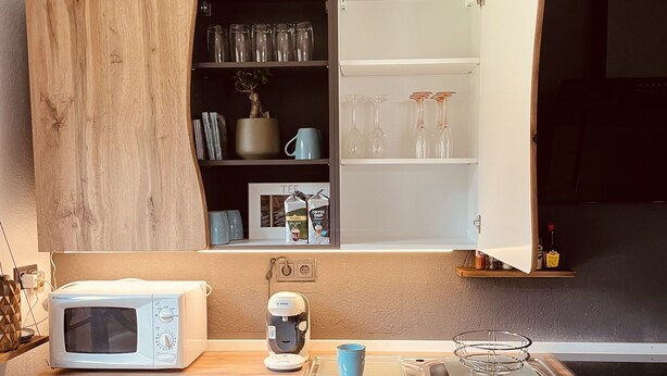 A compact kitchen with a microwave, coffee maker, and a blue mug on the counter. - New, modern apartment with a great garden, centrally located - Bärs Kuschelhöhle (Gerolstein)