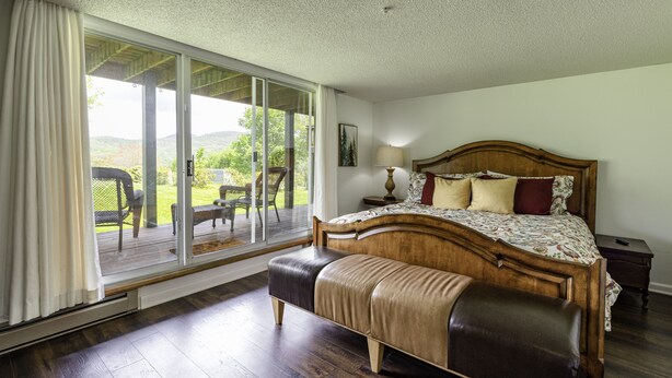 A bedroom with a large bed, a wooden headboard, a nightstand, and a view through a sliding glass door to an outdoor patio. - Your ultimate Sugar Mountain getaway - just steps from the slopes. (Sugar Mountain)