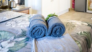 Ein Zimmer mit Bett, einem Fenster mit Jalousien, einer Küchenzeile und einem Deckenventilator.