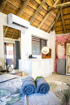 A room with a bed, a window with blinds, a kitchenette, and a ceiling fan.