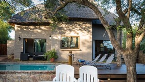 Ein modernes Haus mit Pool, weißen Stühlen und einem Esstisch mit Speisen.